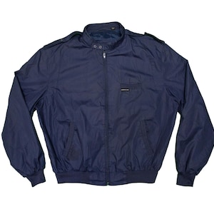 Può includere: Giacca blu navy con zip, piccola tasca sul petto e collo alto. La giacca ha orlo e polsini a coste. Il marchio "Members Only" è visibile sulla tasca sul petto.