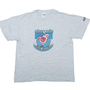Peut inclure: T-shirt gris avec un graphique de Père Noël faisant du patin à glace avec le texte "Santa's Ice Palace".