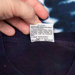 May include: A dark blue tie-dye t-shirt with a white tag attached. The tag includes washing instructions and the text "MADE IN U.S.A."