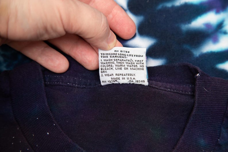 May include: A dark blue tie-dye t-shirt with a white tag attached. The tag includes washing instructions and the text "MADE IN U.S.A."
