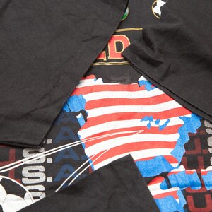 K&ouml;nnte beinhalten: Schwarzes T-Shirt mit einem Grafikdruck eines Fu&szlig;balls, den Worten "U.S.A." und einer stilisierten Karte der Vereinigten Staaten mit roten und wei&szlig;en Streifen.