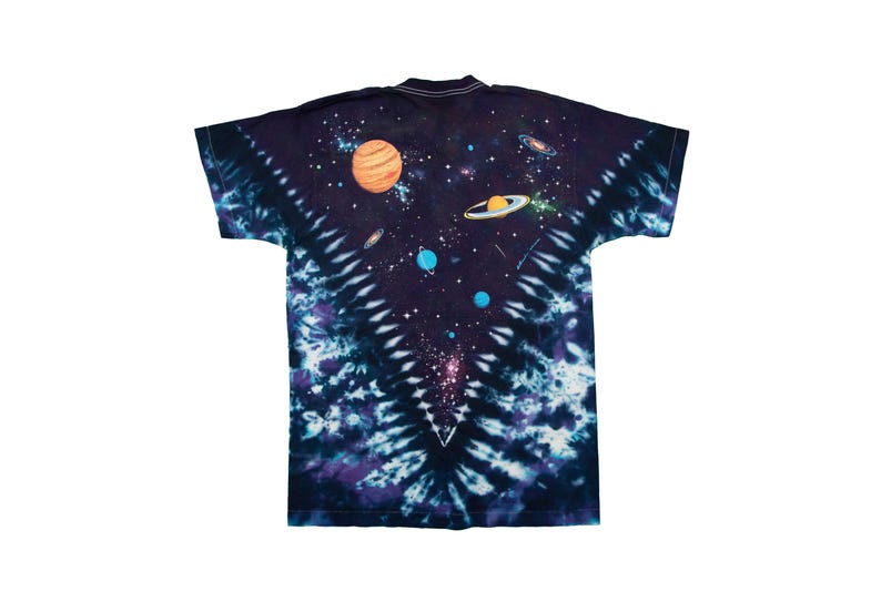 May include: A tie-dye t-shirt featuring a vibrant space-themed design. The shirt showcases planets, galaxies, and stars against a dark blue and purple background. The design is centered on the back of the shirt.