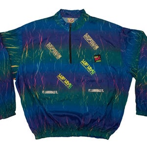 May include: A vintage windbreaker in shades of blue, green, and purple, with a half-zip design. The jacket is emblazoned with the text "SURF STYLE" and includes a small logo, along with the text "FT. LAUDERDALE FL."