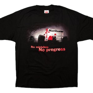 May include: Black t-shirt featuring a racing car with the Marlboro logo. The image shows the car in motion with a spray effect. The text "No mistakes, No progress" is printed in red below the car.