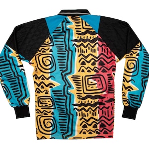 May include: Long-sleeved shirt with a vibrant geometric pattern in teal, yellow, red, and black. The shirt features a black collar and sleeves, with a bold, abstract design across the body. The cuffs are black.