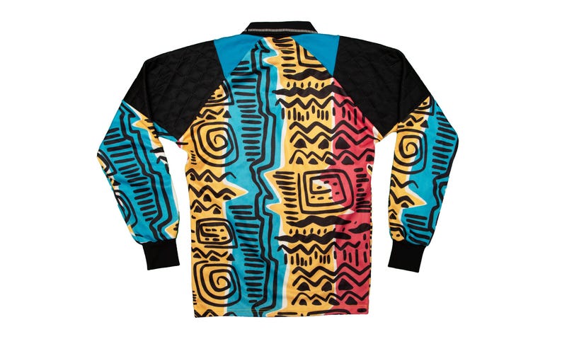 May include: Long-sleeved shirt with a vibrant geometric pattern in teal, yellow, red, and black. The shirt features a black collar and sleeves, with a bold, abstract design across the body. The cuffs are black.