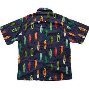 May include: Dark blue short-sleeved button-down shirt with a pattern of colorful surfboards. The surfboards are in various colors, including red, yellow, green, and white. The shirt has a classic collar and is made of a lightweight fabric.