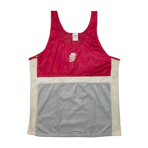 May include: A sleeveless athletic vest in red, white, and grey. The vest features a red upper section, a white horizontal band, and a grey lower section. The Nike logo is visible on the chest.