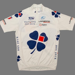 May include: White cycling jersey with blue and red cloverleaf graphics. Features the text "FRANCAISE DES JEUX" and "Lapierre" branding. Includes a partial zipper and short sleeves. The jersey is designed for cycling.
