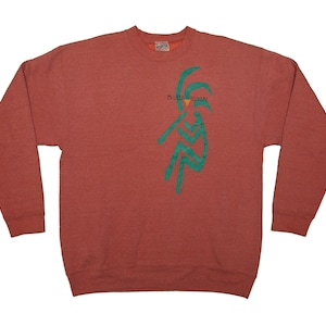 May include: A brick-red sweatshirt with long sleeves. A teal graphic of a person playing a flute is on the front. The text "B. B. Music" is above the graphic. The sweatshirt has a crew neck and ribbed cuffs.