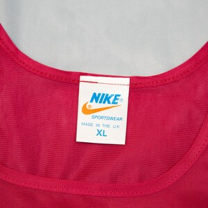 May include: A red vest top with a rounded neckline. A white label displays the Nike logo, the word "Sportswear", and "Made in the U.K." The size is XL.
