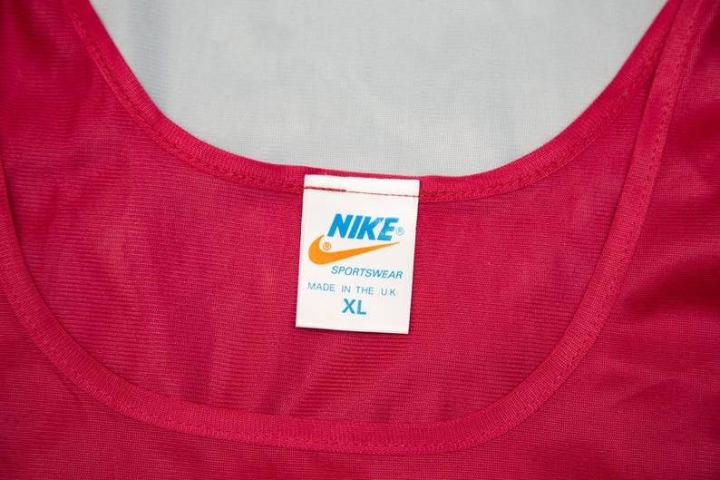 May include: A red vest top with a rounded neckline. A white label displays the Nike logo, the word "Sportswear", and "Made in the U.K." The size is XL.