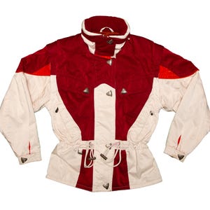 May include: A vintage ski jacket in a colour block design. The jacket features a red upper section and white sleeves and lower body. It has a high collar, silver-tone buttons, and a drawstring waist. The jacket is a retro style.