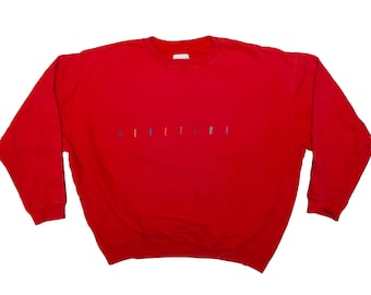 May include: A vibrant red sweatshirt with long sleeves. The word "DEFINITION" is embroidered in small, multi-coloured letters across the chest. The sweatshirt has a crew neck and is a solid colour.