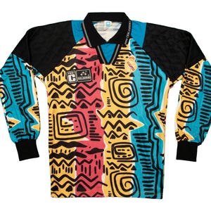 May include: A long-sleeved jersey with a vibrant, abstract pattern. The shirt features a black collar and sleeves, with a colorful design of yellow, red, and blue shapes. The jersey has a V-neck and includes patches with text.