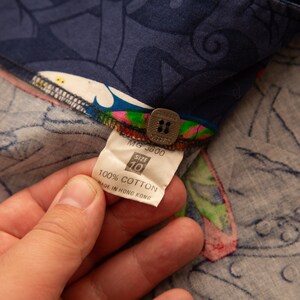 May include: Close-up of a navy blue fabric with a colorful floral pattern. The fabric has a tag that reads "100% Cotton" and "Made in Hong Kong". The tag also indicates a size 10.