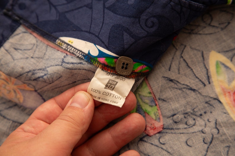 May include: Close-up of a navy blue fabric with a colorful floral pattern. The fabric has a tag that reads "100% Cotton" and "Made in Hong Kong". The tag also indicates a size 10.