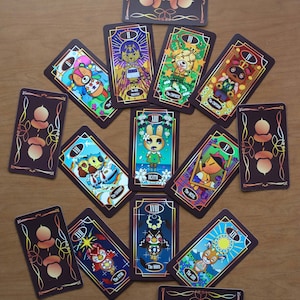 May include: A deck of tarot cards featuring colorful illustrations of animal characters. Each card has a dark brown border with gold accents and a unique design. The cards are arranged in a circular pattern on a wooden surface.