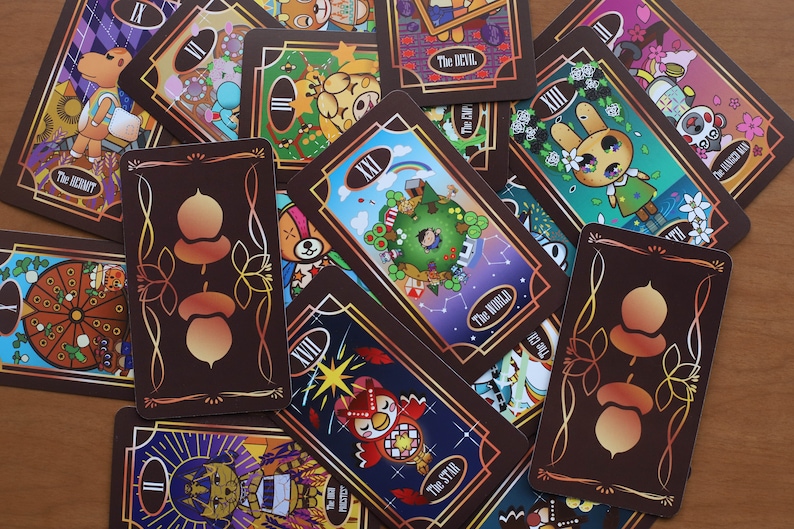 May include: A collection of tarot cards with brown borders and colorful illustrations. The cards feature various designs, including a rabbit, an owl, and a world scene. The backs of the cards have an acorn design. The cards are scattered on a wooden surface.