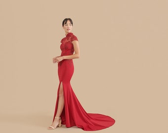 May include: A woman wearing a red, floor-length gown with a high neck and a slit up the side. The gown has delicate lace detailing on the bodice and a train.