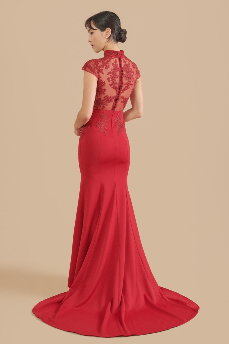 Pode incluir: Um vestido vermelho longo at&eacute; o ch&atilde;o com um corpete justo e uma saia fluida. O corpete apresenta uma sobreposi&ccedil;&atilde;o de renda transparente com bordados florais e um decote alto. A parte de tr&aacute;s do vestido tem uma fila de bot&otilde;es.