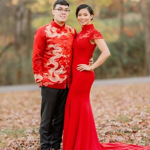 Pode incluir: Um casal com trajes tradicionais de casamento chin&ecirc;s. O homem est&aacute; vestindo uma jaqueta vermelha com bordados de drag&otilde;es dourados e cal&ccedil;as pretas. A mulher est&aacute; vestindo um vestido vermelho com gola alta e uma cauda longa. Eles est&atilde;o em p&eacute; em um campo de folhas ca&iacute;das.