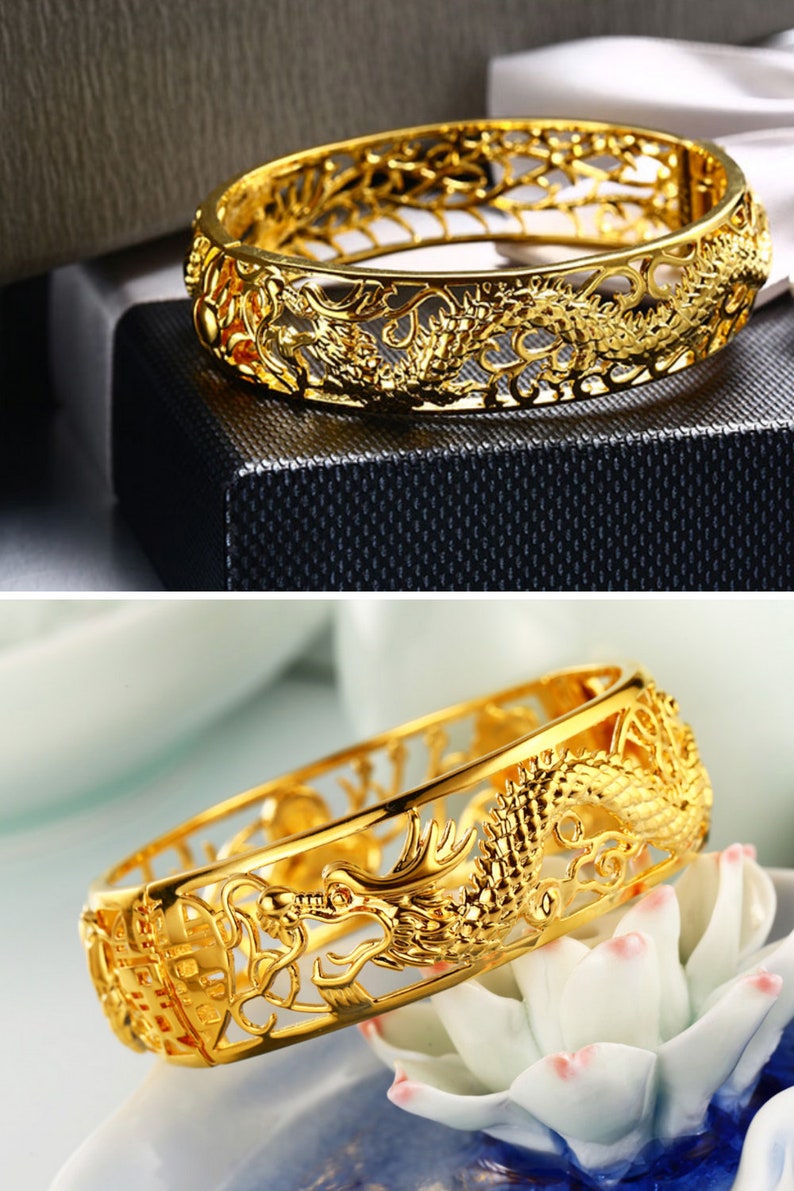 May include: A gold-colored bracelet with a dragon design. The bracelet is made of a shiny, metallic material and features intricate cut-out details. The dragon is a prominent feature, with detailed scales and a flowing design. The bracelet is a cuff style.