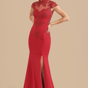 Pode incluir: Um vestido vermelho longo at&eacute; o ch&atilde;o com gola alta e mangas curtas. O vestido tem um corpete justo e uma saia fluida com uma fenda na frente. O vestido &eacute; decorado com bordados delicados.