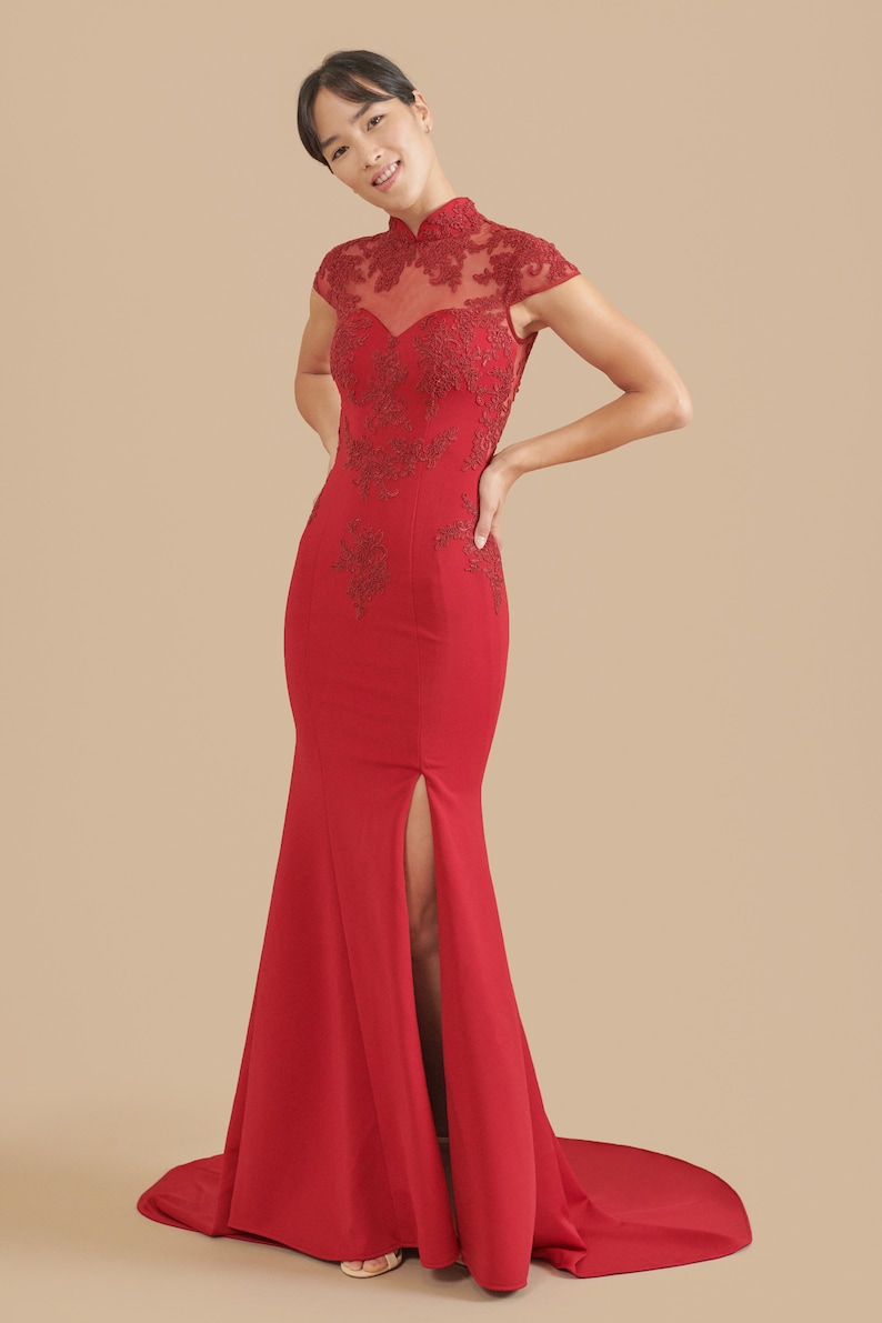 Pode incluir: Um vestido vermelho longo at&eacute; o ch&atilde;o com gola alta e mangas curtas. O vestido tem um corpete justo e uma saia fluida com uma fenda na frente. O vestido &eacute; decorado com bordados delicados.