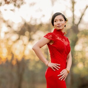 Pode incluir: Uma mulher com um vestido vermelho com bordados intrincados est&aacute; em um ambiente de floresta. O vestido tem um colar alto e mangas curtas. A mulher est&aacute; olhando para o lado, com o cabelo puxado para tr&aacute;s.