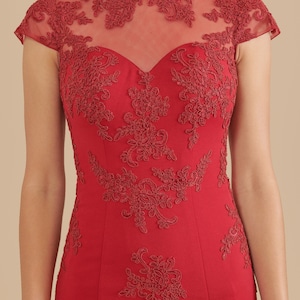 Pode incluir: Um vestido vermelho com decote alto e mangas curtas. O vestido &eacute; feito de um tecido transparente com bordados de renda floral.