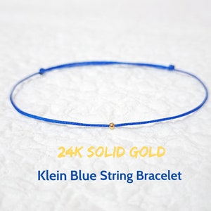 Op de afbeelding: Een blauw koord armbandje met een klein gouden kraaltje. 24K Solid Gold Klein Blue String Bracelet.