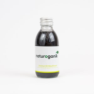 Könnte beinhalten: Eine durchsichtige Glasflasche mit einer schwarzen Flüssigkeit. Die Flasche hat einen silbernen Deckel und ein weißes Etikett mit dem Text "naturoganik" und "Coconut Oil Mouthwash with Charcoal & Spearmint Extract".