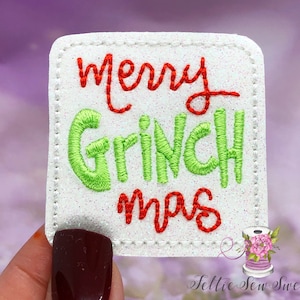 May include: A white, square patch with the embroidered text "Merry Grinchmas" in red and green. The patch has a glittery texture and a stitched border. A small logo is visible in the bottom right corner.