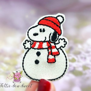 May include: White felt snowman applique with a red and white striped scarf and a red hat. The snowman has black eyes and a black mouth.