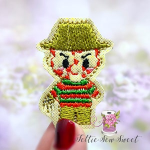 May include: Embroidered iron-on patch featuring a cartoon character with a green and red striped shirt, a brown hat, and a menacing expression.