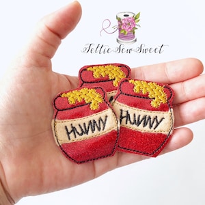 May include: Three red felt honey pot appliques with yellow felt honey and black embroidered text. The text on the appliques reads "HONEY" and "HUNNY".