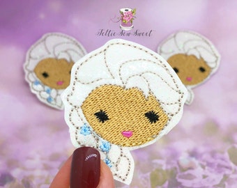 May include: White felt applique with a glittery finish, featuring a cartoon face with brown skin, black eyes, and pink lips. The applique is surrounded by a white border with blue flowers.