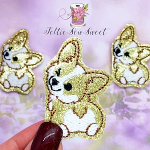 May include: Three gold glitter embroidered patches of a cartoon corgi dog. The corgi is white with gold glitter fur and black eyes. The patches are approximately 2 inches in size.