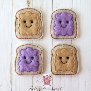 May include: Four felt appliques of peanut butter and jelly sandwiches. Each sandwich has a smiling face and is made of brown and purple felt.