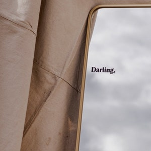 May include: A gold-framed mirror with a cloudy sky reflected in the glass. The word "Darling" is written in black lettering on the mirror.