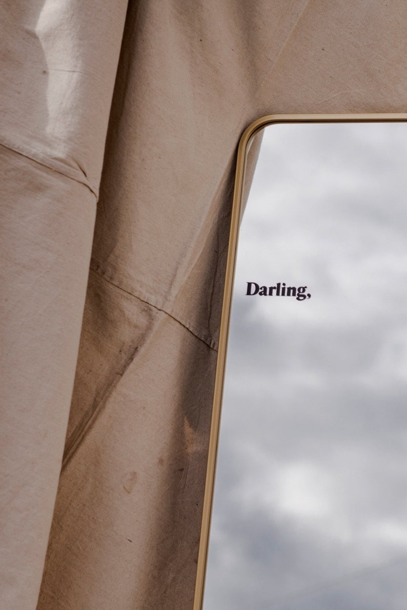 May include: A gold-framed mirror with a cloudy sky reflected in the glass. The word "Darling" is written in black lettering on the mirror.