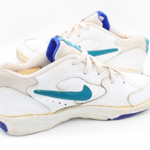 May include: White leather sneakers with a blue and teal swoosh logo. The shoes have a white sole with a blue trim.