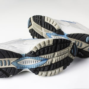 May include: A pair of white athletic shoes with blue accents on the soles. The shoes are worn and have a textured sole.