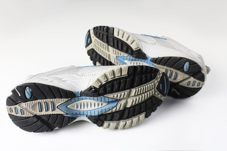 May include: A pair of white athletic shoes with blue accents on the soles. The shoes are worn and have a textured sole.