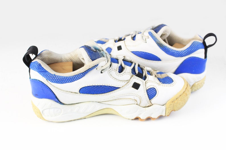 Może przedstawiać: Para białych i niebieskich but&oacute;w sportowych z grubą podeszwą. Buty mają niebieski panel z siatki i białą sk&oacute;rzaną cholewkę.