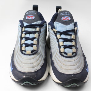 May include: A pair of blue and gray Nike cross training sneakers with a white background. The shoes have a black and blue lace-up closure and the text "CROSS TRAINING" on the tongue.
