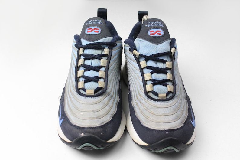May include: A pair of blue and gray Nike cross training sneakers with a white background. The shoes have a black and blue lace-up closure and the text "CROSS TRAINING" on the tongue.