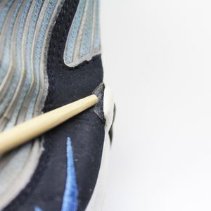 May include: Close-up of a blue and gray running shoe with a black and blue swoosh logo. A wooden chopstick is resting on the shoe.