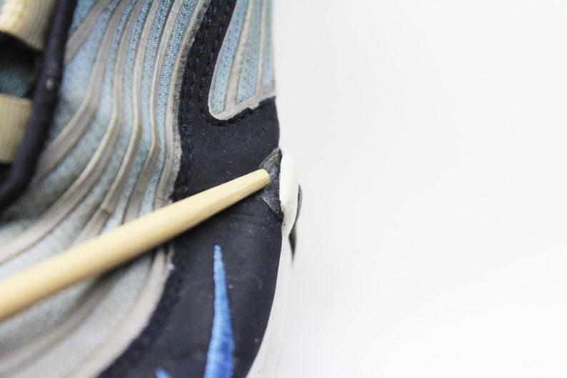 May include: Close-up of a blue and gray running shoe with a black and blue swoosh logo. A wooden chopstick is resting on the shoe.